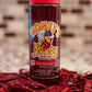 Bottle of Honey's Hot Honey with red cap on a surface with dried red chili de arbol pepper.