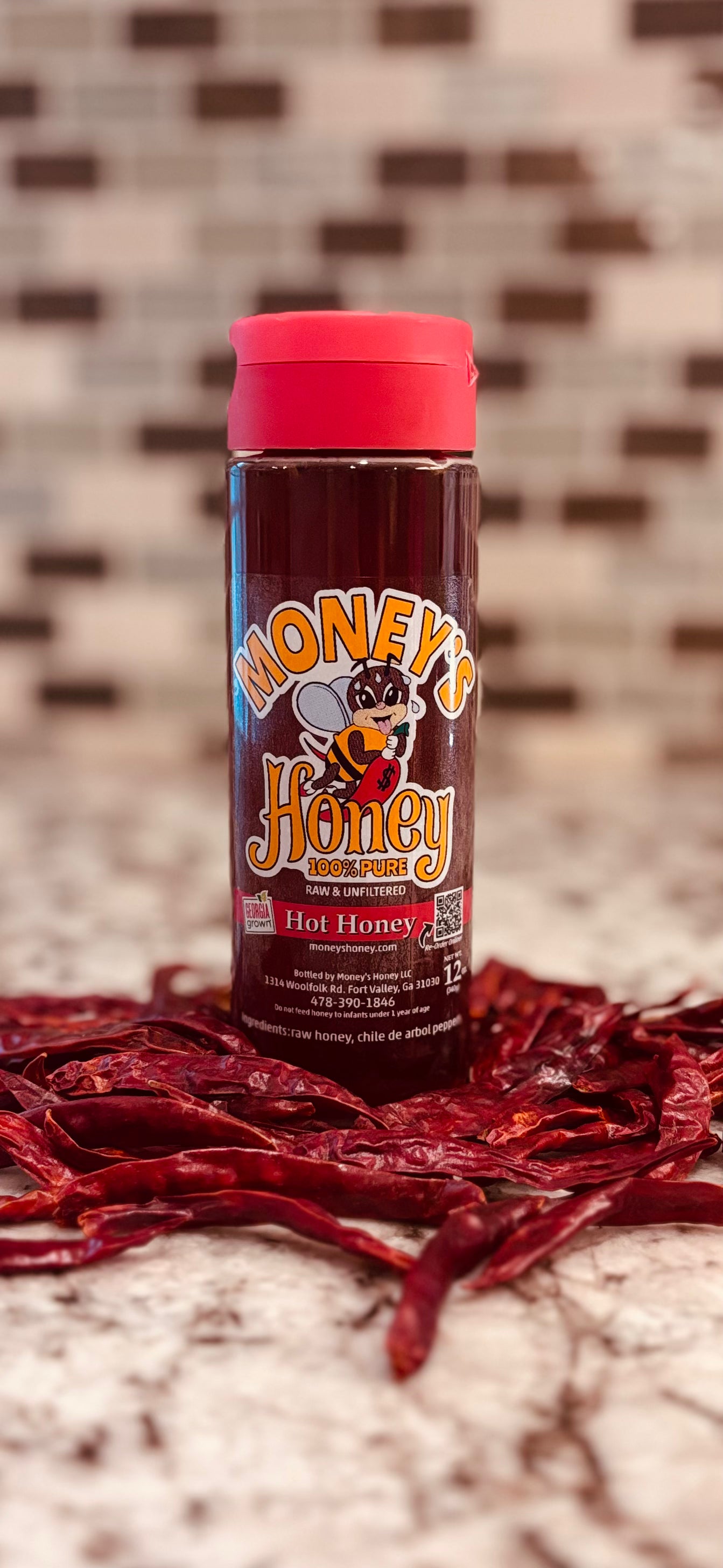 Bottle of Honey's Hot Honey with red cap on a surface with dried red chili de arbol pepper.