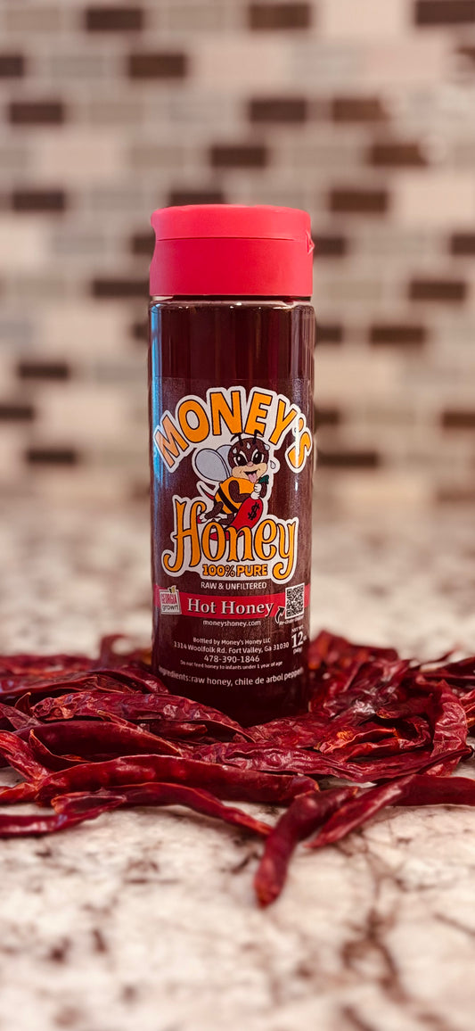 Bottle of Honey's Hot Honey with red cap on a surface with dried red chili de arbol pepper.